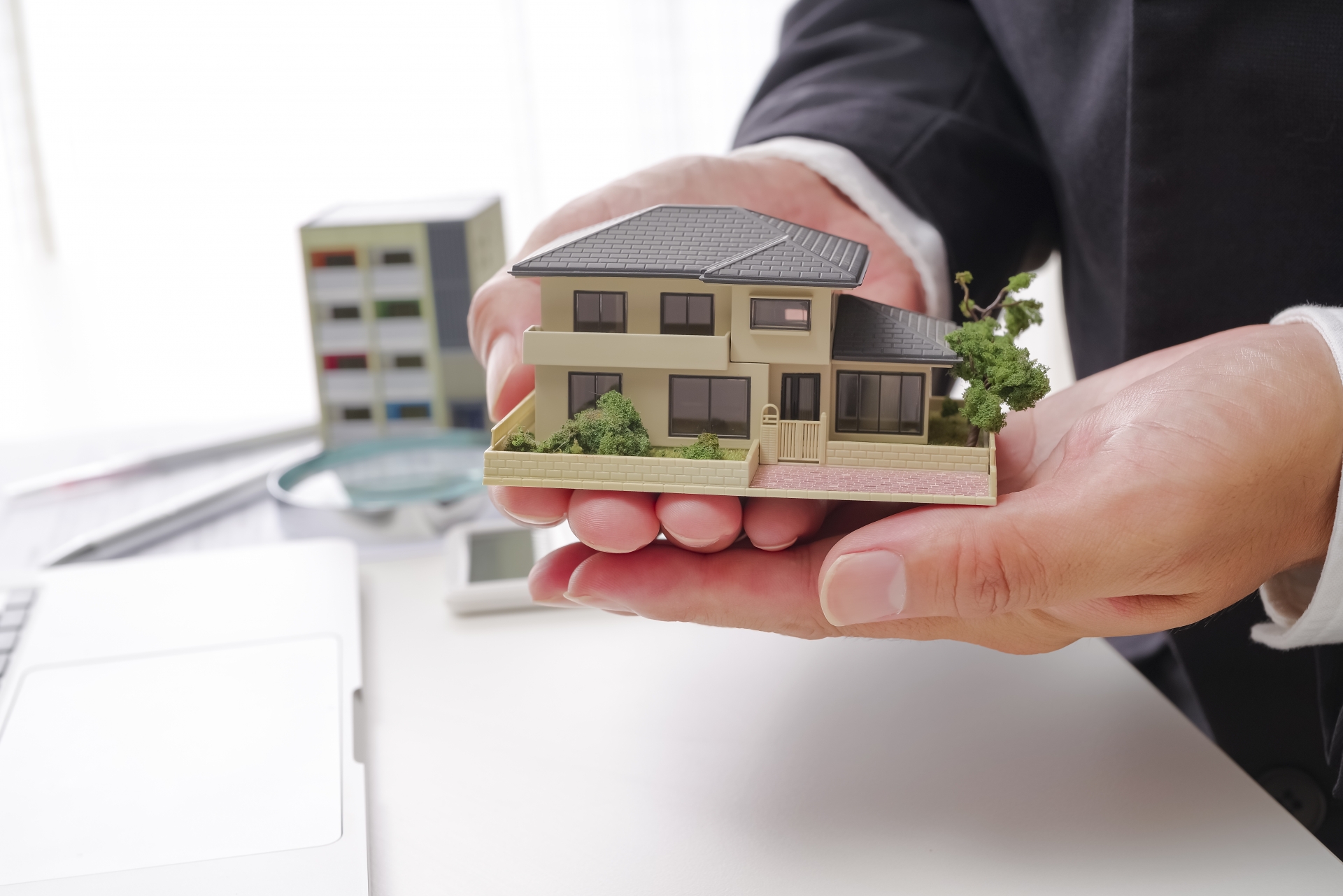 不動産売却や購入の引き渡しをイメージさせる、精巧な戸建て模型を差し出す手元