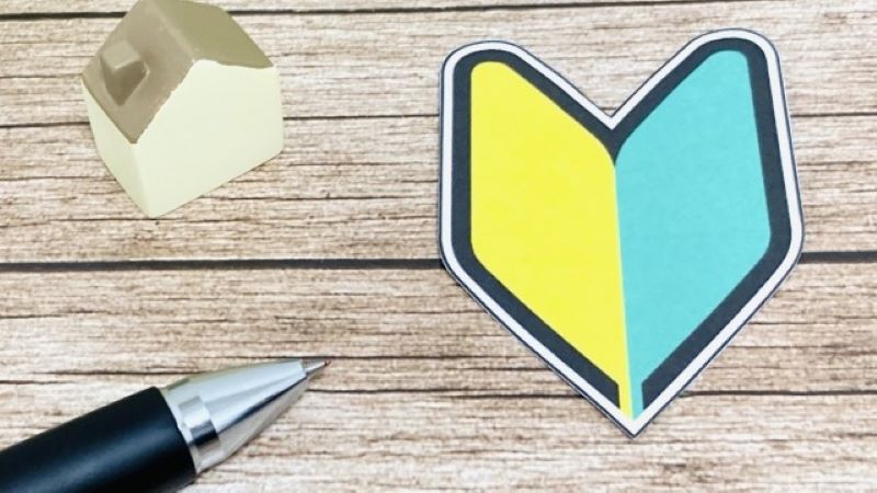 オウンドメディアの戦略立案を始める初心者のための基礎知識をイメージし、木目テーブルの上に初心者マークと文房具、家の模型を並べた様子。