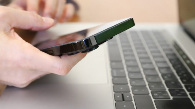 オウンドメディア集客に役立つツールを操作するため、パソコンの傍らでスマホを扱う手元。